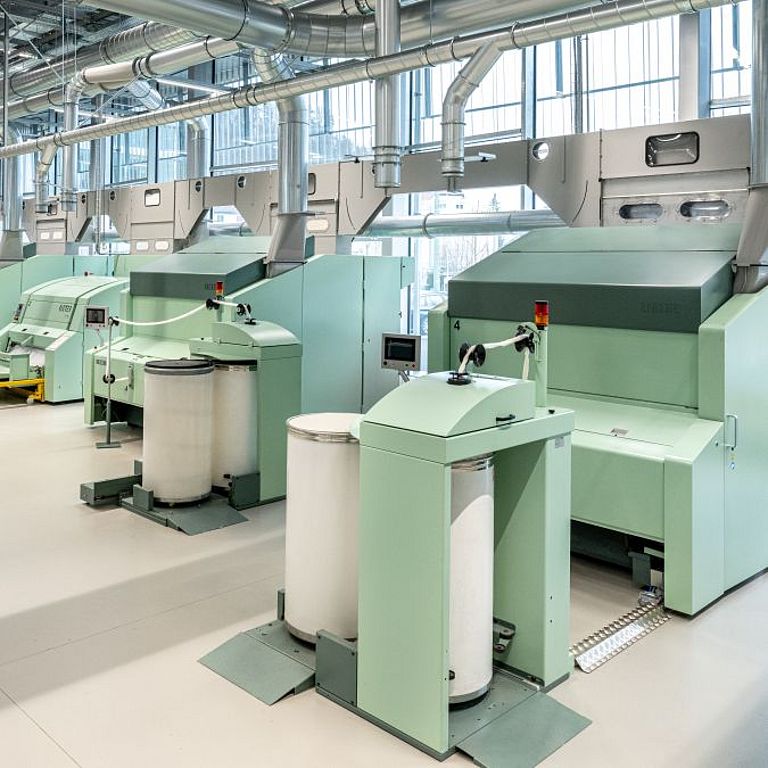 Interior view of the Spin Center at the Rieter Innovation Center in Winterthur, Switzerland. In the foreground, a Rieter expert checks the settings of a card.