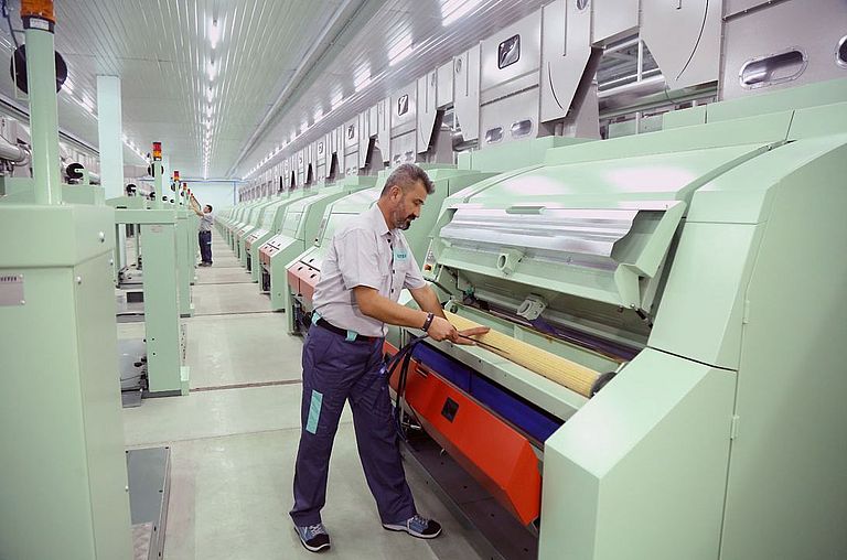 In a spinning mill, many cards side by side, a Rieter employee checks the settings of a card