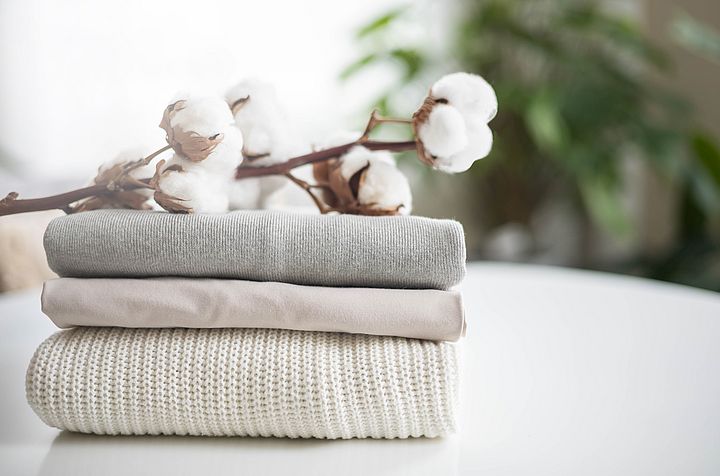 Knitwear from recycled textiles A neat stack of clean knitwear in neutral colors. Concept for sale, recycling and storage of clothing. Branch of cotton inflorescences.