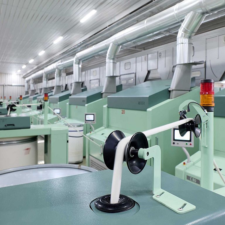 纱厂中的多台梳棉机，焦点对准其中一台梳棉机生产的棉条