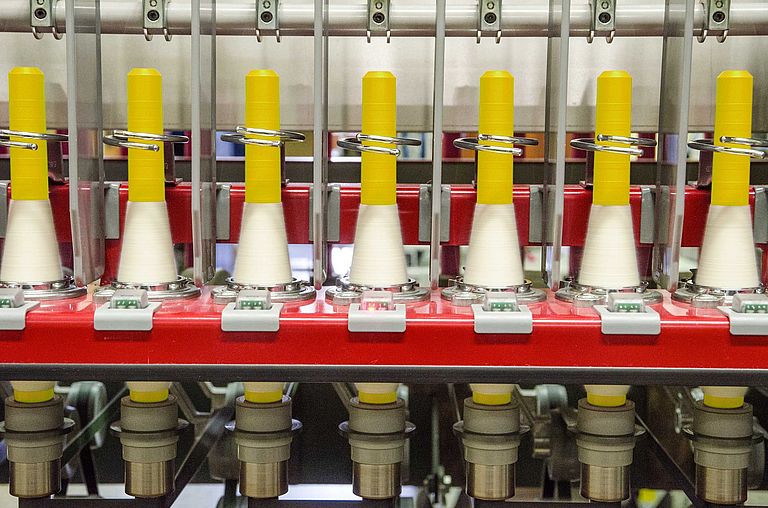 Sechs Spinnstellen einer Ringspinnmaschine mit LEDs an jeder Spinnstelle. Eine LED leuchtet rot.