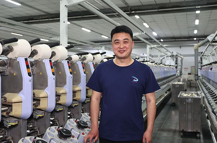 Zhang Sheng, Chief Engineer bei Sanyang Textile Co., Ltd., steht nach der Installation des Saugdüsen-Upgrades vor der Spulmaschine Autoconer 338.