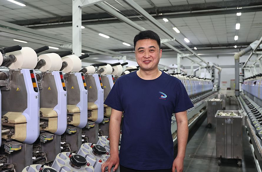 Zhang Sheng, Chief Engineer bei Sanyang Textile Co., Ltd., steht nach der Installation des Saugdüsen-Upgrades vor der Spulmaschine Autoconer 338.