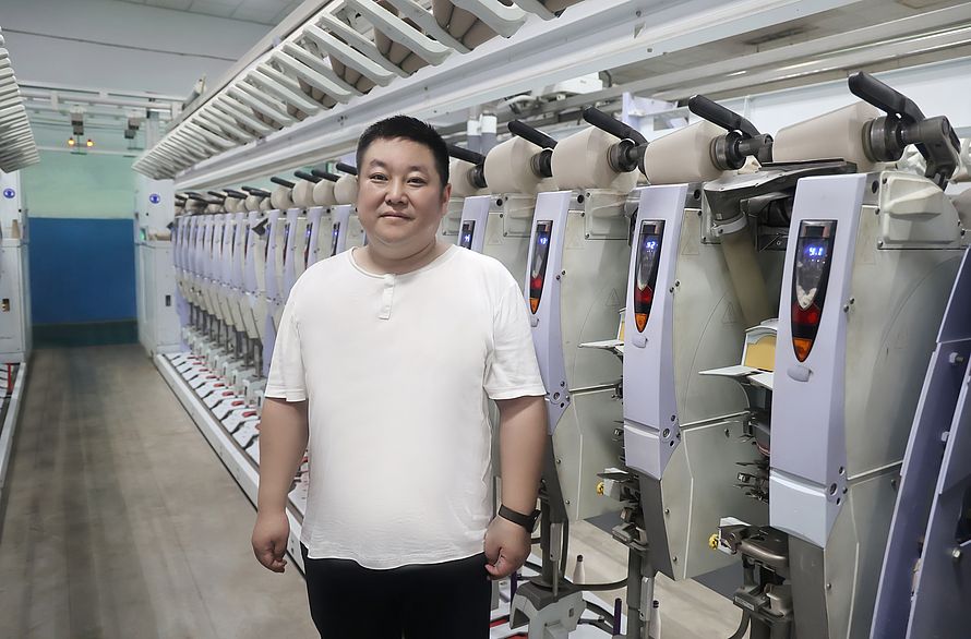 Chefingenieur Wang Ping im Werk von Wugang Longshan Textile vor Spulmaschinen Autoconer X5, die mit der Smartjet-Power-Düsentechnologie ausgerüstet wurden.